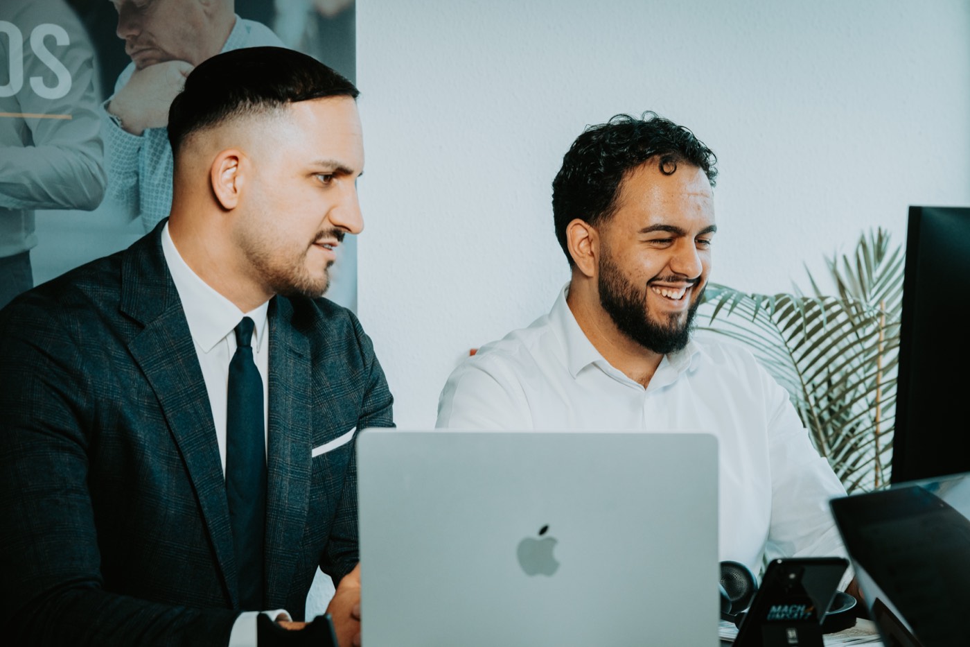 Zwei Kollegen von Umsatz mit Autos arbeiten gemeinsam am MacBook im modernen Büro in Lörrach
